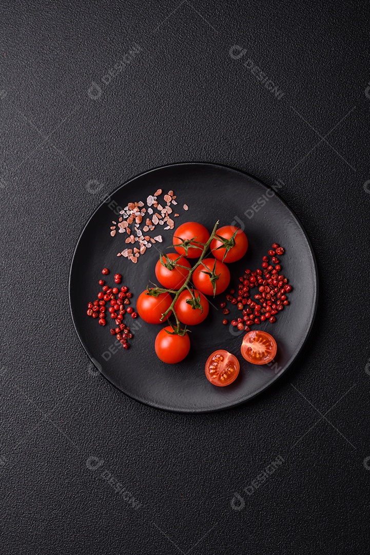 Um ramo de tomate cereja cru com sal e especiarias sobre um fundo escuro. Ingredientes para cozinhar em casa
