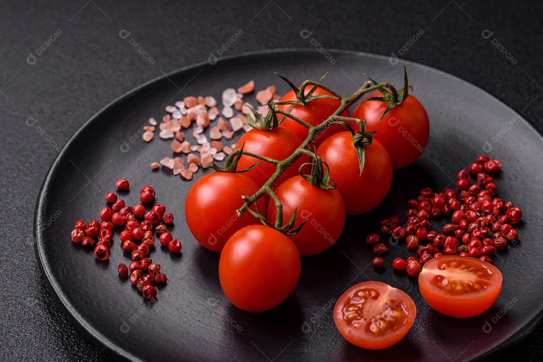 Um ramo de tomate cereja cru com sal e especiarias sobre um fundo escuro. Ingredientes para cozinhar em casa