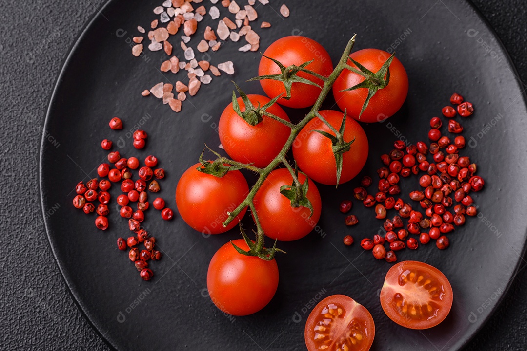 Um ramo de tomate cereja cru com sal e especiarias sobre um fundo escuro. Ingredientes para cozinhar em casa