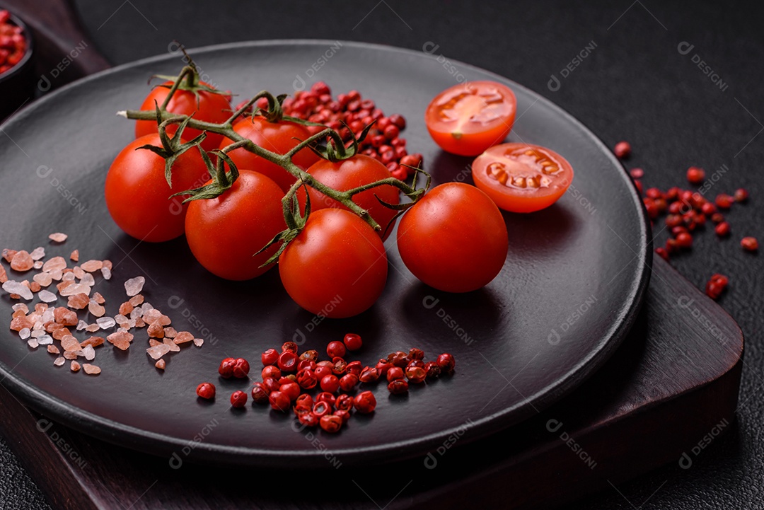 Um ramo de tomate cereja cru com sal e especiarias sobre um fundo escuro. Ingredientes para cozinhar em casa