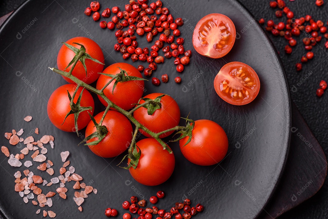 Um ramo de tomate cereja cru com sal e especiarias sobre um fundo escuro. Ingredientes para cozinhar em casa