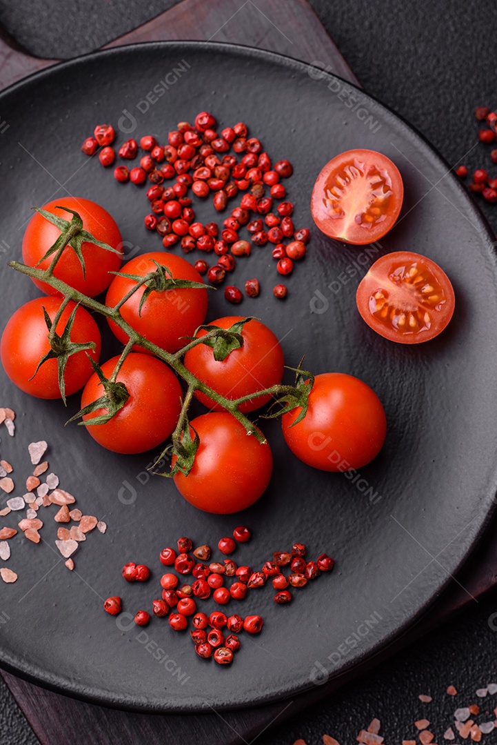 Um ramo de tomate cereja cru com sal e especiarias sobre um fundo escuro. Ingredientes para cozinhar em casa