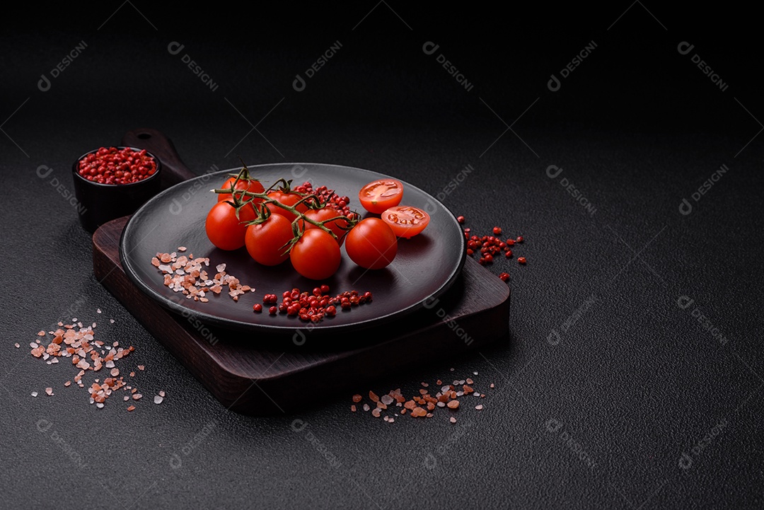 Um ramo de tomate cereja cru com sal e especiarias sobre um fundo escuro. Ingredientes para cozinhar em casa