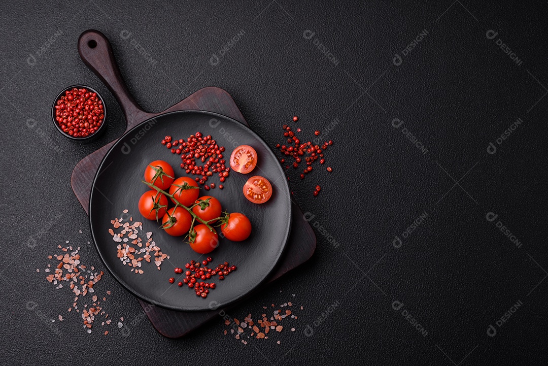 Um ramo de tomate cereja cru com sal e especiarias sobre um fundo escuro. Ingredientes para cozinhar em casa