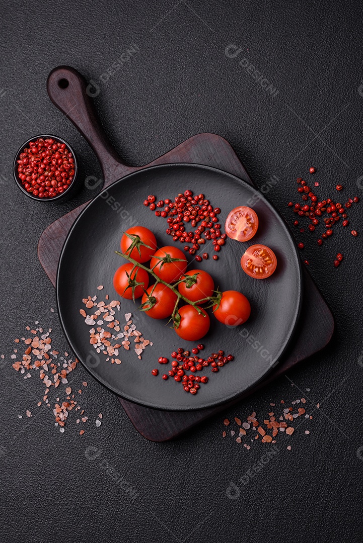 Um ramo de tomate cereja cru com sal e especiarias sobre um fundo escuro. Ingredientes para cozinhar em casa