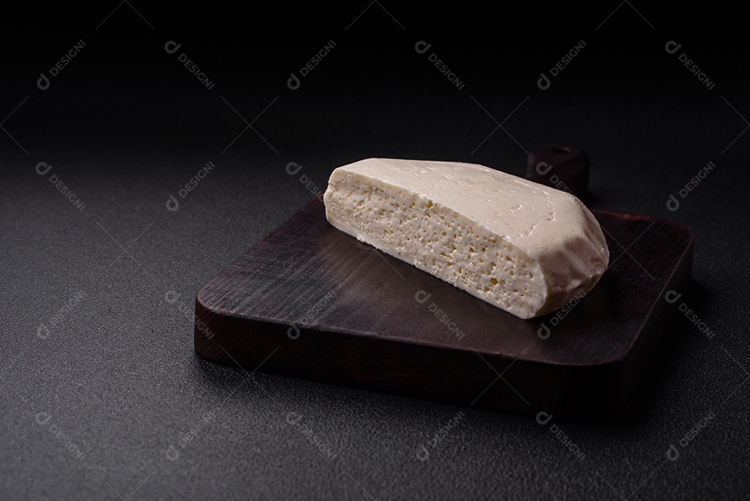 Delicioso queijo jovem branco fresco de leite de vaca ou ovelha sobre um fundo escuro de concreto