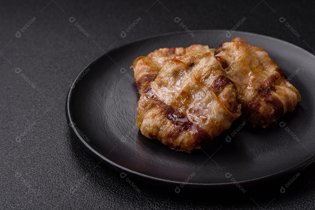 Frango picado redondo ou costeleta de porco envolta em bacon com sal, especiarias e ervas sobre um fundo escuro de concreto