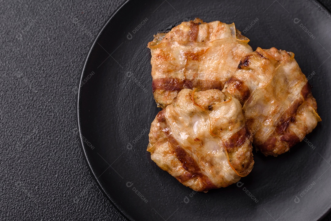 Frango picado redondo ou costeleta de porco envolta em bacon com sal, especiarias e ervas sobre um fundo escuro de concreto
