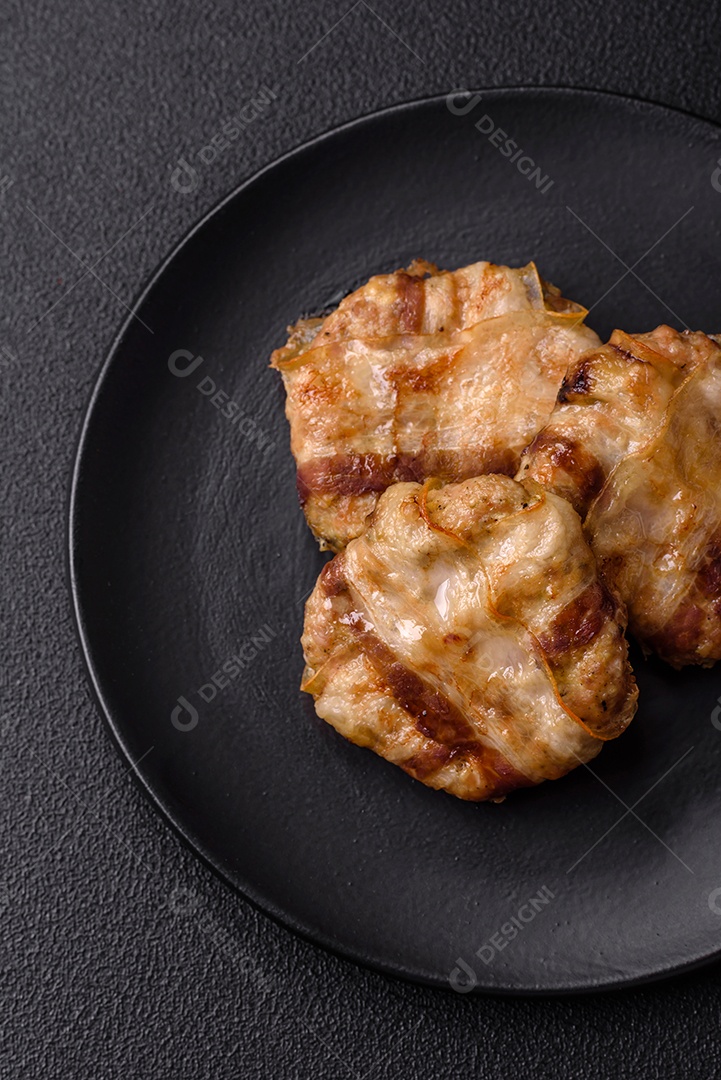 Frango picado redondo ou costeleta de porco envolta em bacon com sal, especiarias e ervas sobre um fundo escuro de concreto
