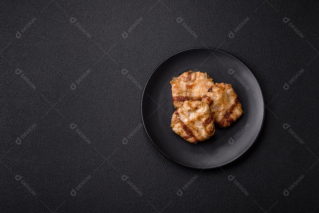 Frango picado redondo ou costeleta de porco envolta em bacon com sal, especiarias e ervas sobre um fundo escuro de concreto