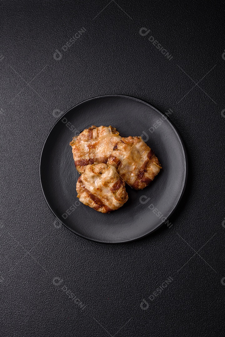 Frango picado redondo ou costeleta de porco envolta em bacon com sal, especiarias e ervas sobre um fundo escuro de concreto