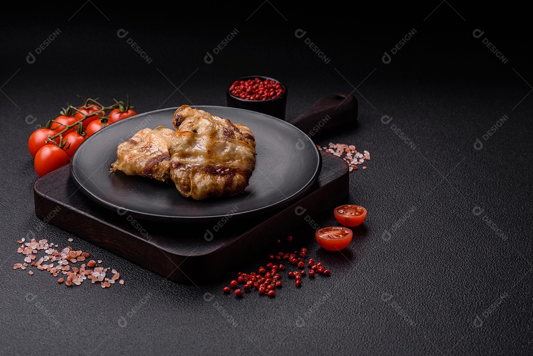 Frango picado redondo ou costeleta de porco envolta em bacon com sal, especiarias e ervas sobre um fundo escuro de concreto