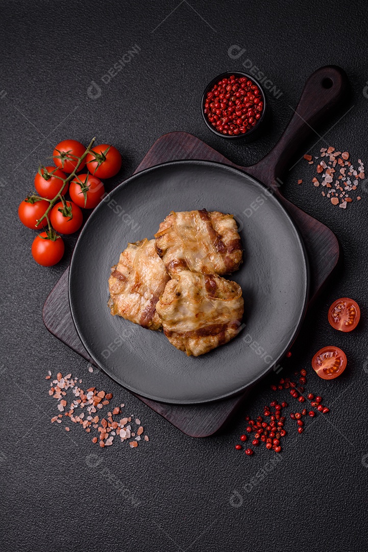 Frango picado redondo ou costeleta de porco envolta em bacon com sal, especiarias e ervas sobre um fundo escuro de concreto