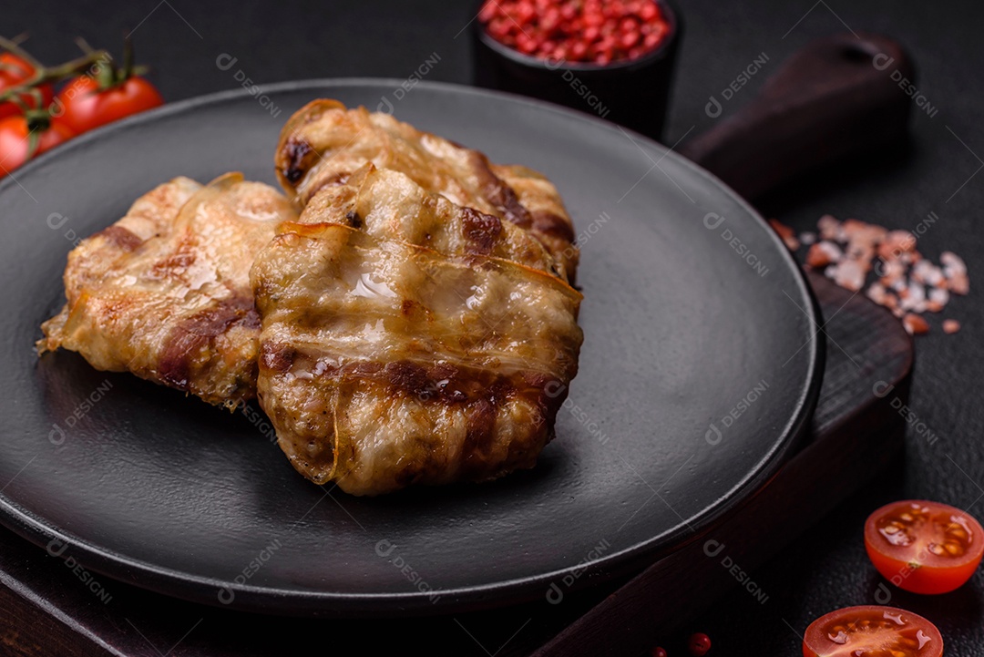 Frango picado redondo ou costeleta de porco envolta em bacon com sal, especiarias e ervas sobre um fundo escuro de concreto