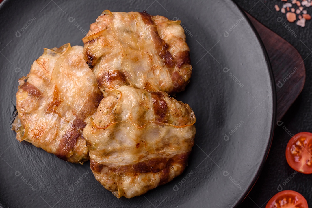 Frango picado redondo ou costeleta de porco envolta em bacon com sal, especiarias e ervas sobre um fundo escuro de concreto