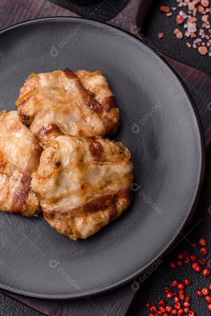 Frango picado redondo ou costeleta de porco envolta em bacon com sal, especiarias e ervas sobre um fundo escuro de concreto