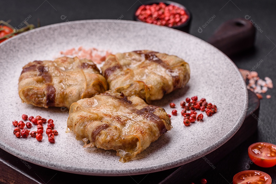Frango picado redondo ou costeleta de porco envolta em bacon com sal, especiarias e ervas sobre um fundo escuro de concreto