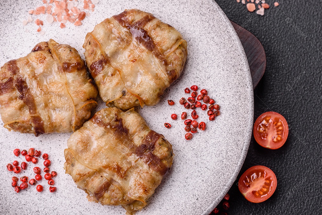 Frango picado redondo ou costeleta de porco envolta em bacon com sal, especiarias e ervas sobre um fundo escuro de concreto