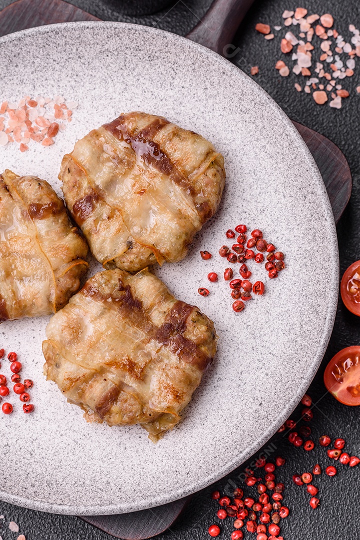 Frango picado redondo ou costeleta de porco envolta em bacon com sal, especiarias e ervas sobre um fundo escuro de concreto