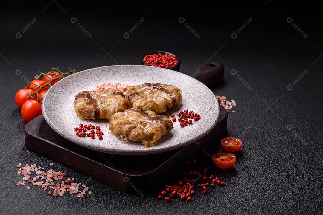 Frango picado redondo ou costeleta de porco envolta em bacon com sal, especiarias e ervas sobre um fundo escuro de concreto