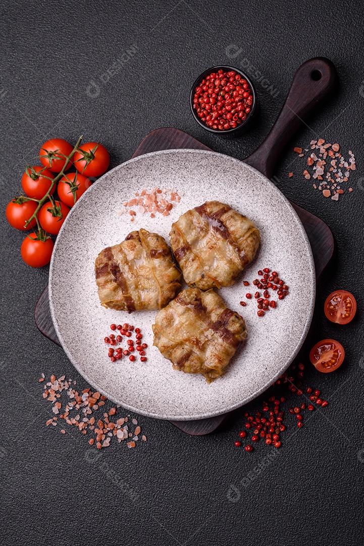 Frango picado redondo ou costeleta de porco envolta em bacon com sal, especiarias e ervas sobre um fundo escuro de concreto