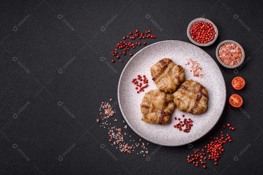 Frango picado redondo ou costeleta de porco envolta em bacon com sal, especiarias e ervas sobre um fundo escuro de concreto