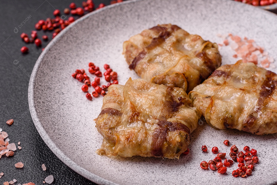 Frango picado redondo ou costeleta de porco envolta em bacon com sal, especiarias e ervas sobre um fundo escuro de concreto