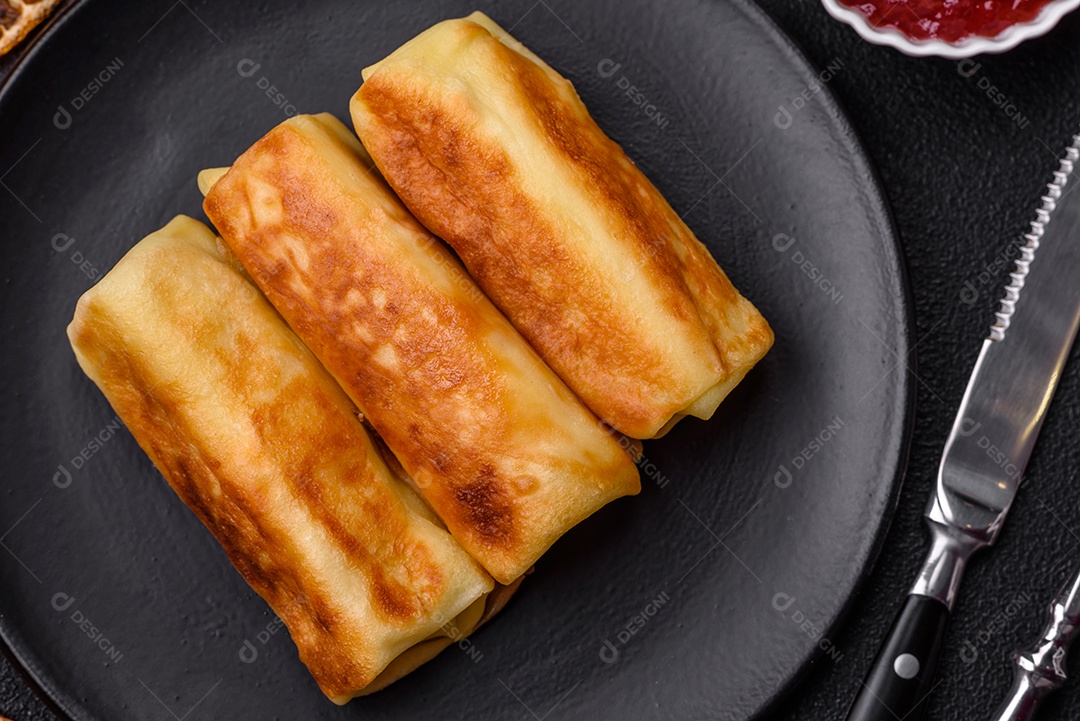 Deliciosas panquecas fritas com recheio roladas sobre um fundo escuro de concreto. Delicioso café da manhã nutritivo