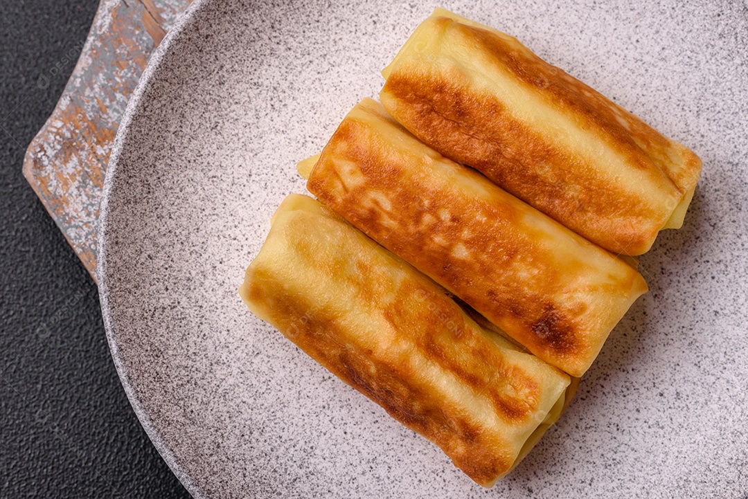 Deliciosas panquecas fritas com recheio roladas sobre um fundo escuro de concreto. Delicioso café da manhã nutritivo