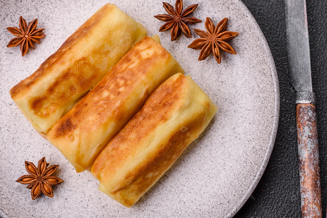 Deliciosas panquecas fritas com recheio roladas sobre um fundo escuro de concreto. Delicioso café da manhã nutritivo