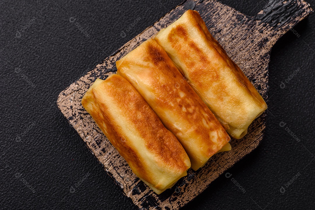 Deliciosas panquecas fritas com recheio roladas sobre um fundo escuro de concreto. Delicioso café da manhã nutritivo