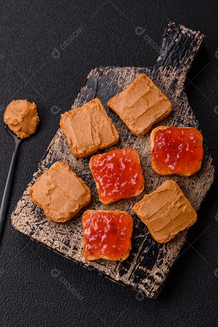 Deliciosos sanduíches nutritivos com manteiga de amendoim, geléia de morango sobre fundo escuro de concreto