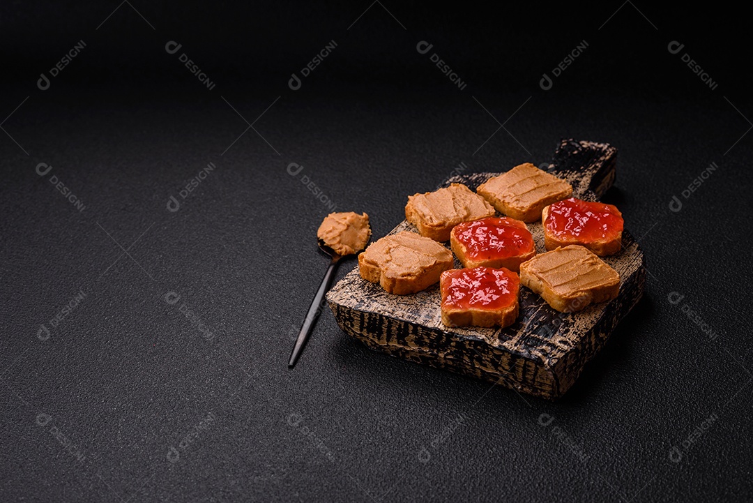 Deliciosos sanduíches nutritivos com manteiga de amendoim, geléia de morango sobre fundo escuro de concreto