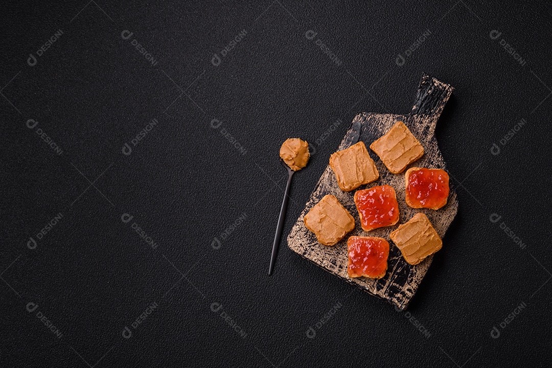 Deliciosos sanduíches nutritivos com manteiga de amendoim, geléia de morango sobre fundo escuro de concreto