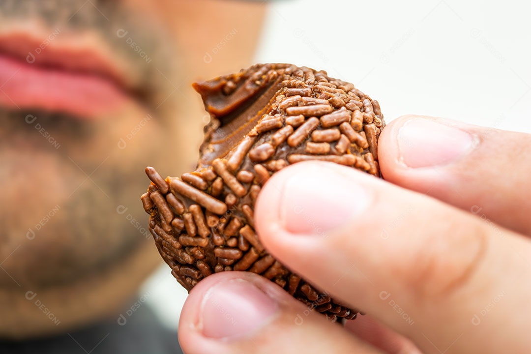Homem com excesso de peso comendo um brigadeiro, sobremesa tradicional brasileira