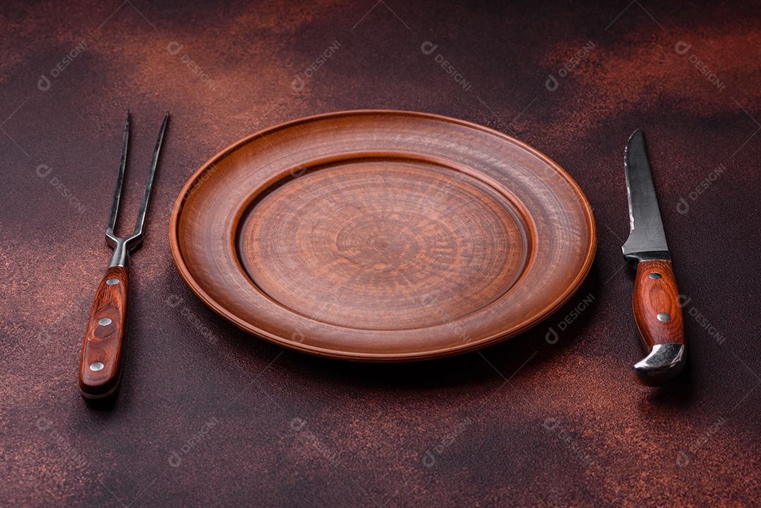 Placa redonda de cerâmica vazia em fundo de concreto texturizado escuro. Talheres, preparação para o jantar
