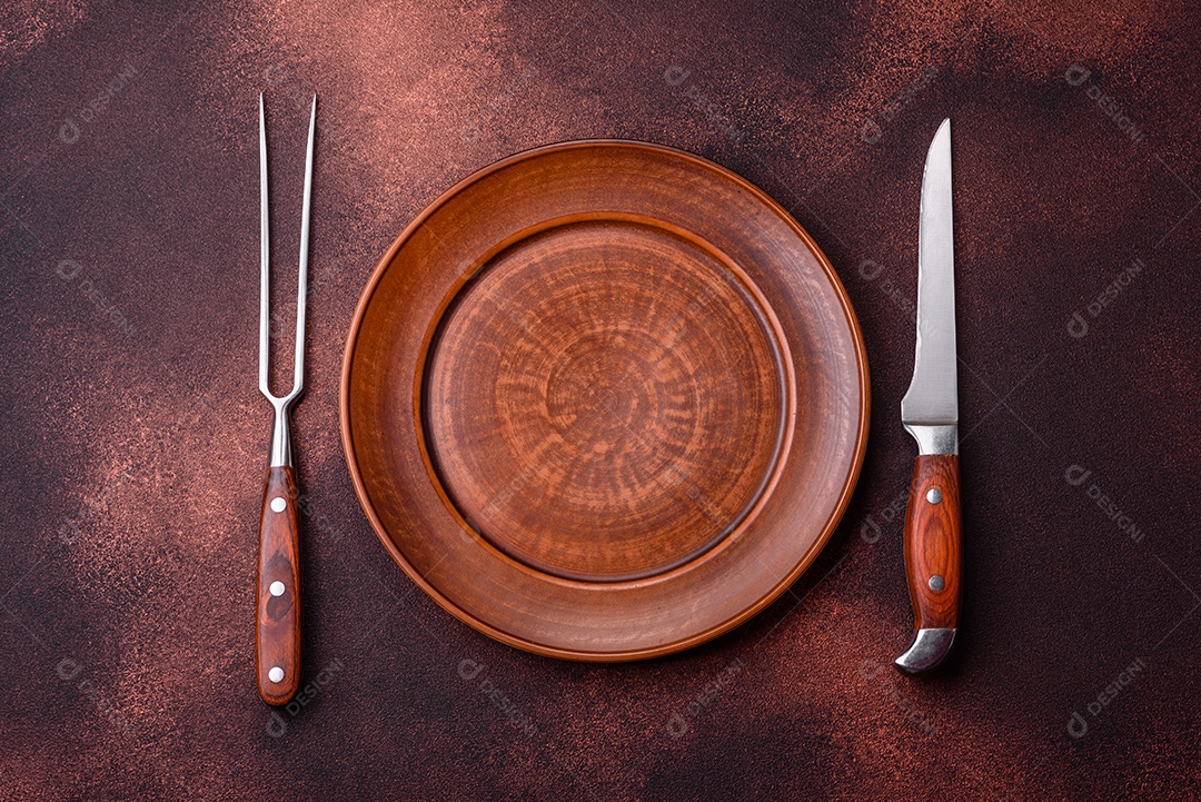 Placa redonda de cerâmica vazia em fundo de concreto texturizado escuro. Talheres, preparação para o jantar