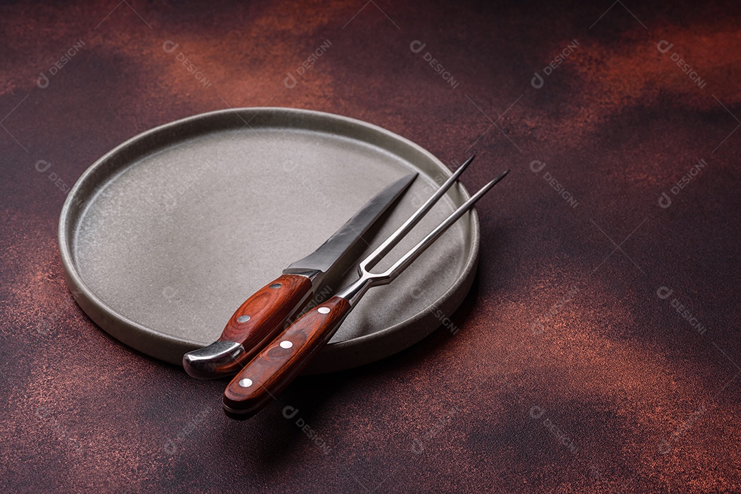 Placa redonda de cerâmica vazia em fundo de concreto texturizado escuro. Talheres, preparação para o jantar