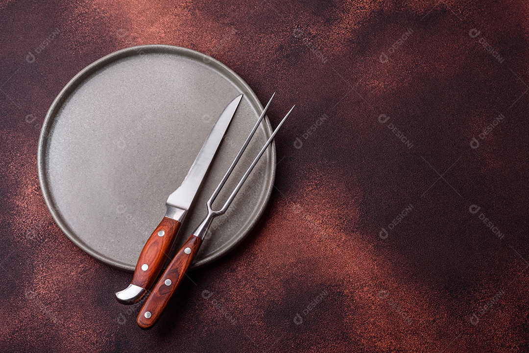 Placa redonda de cerâmica vazia em fundo de concreto texturizado escuro. Talheres, preparação para o jantar