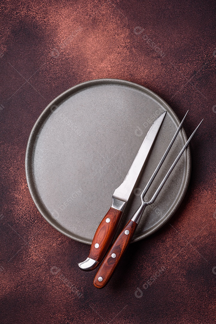 Placa redonda de cerâmica vazia em fundo de concreto texturizado escuro. Talheres, preparação para o jantar