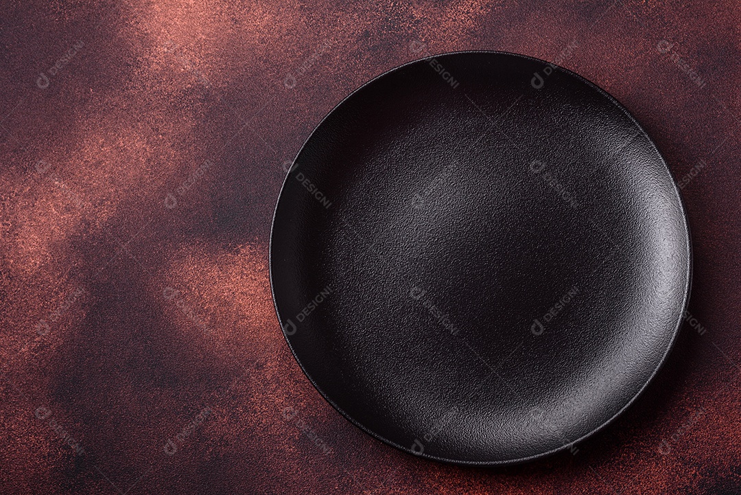 Placa redonda de cerâmica vazia em fundo de concreto texturizado escuro. Talheres, preparação para o jantar