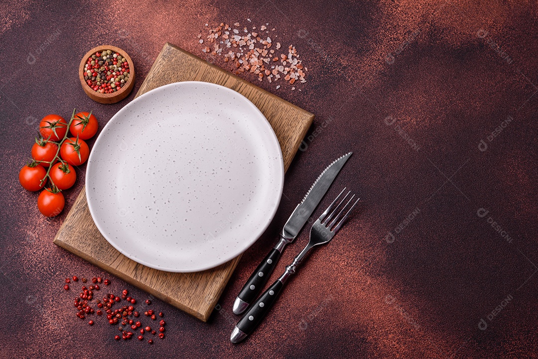 Placa redonda de cerâmica vazia em fundo de concreto texturizado escuro. Talheres, preparação para o jantar