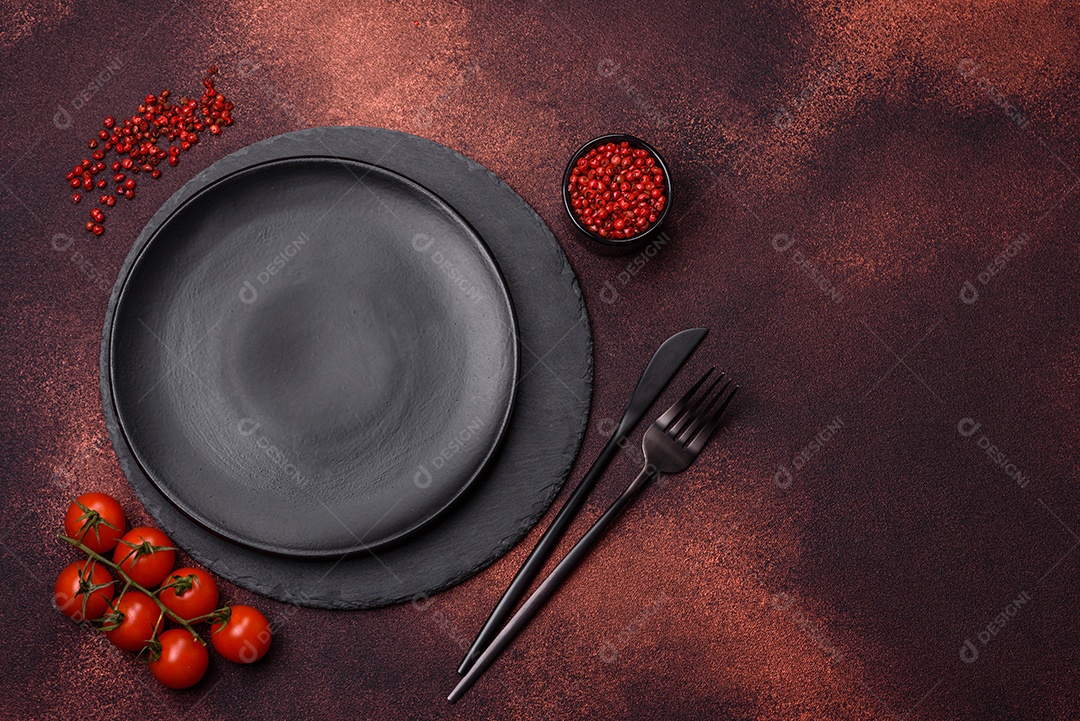 Placa redonda de cerâmica vazia em fundo de concreto texturizado escuro. Talheres, preparação para o jantar
