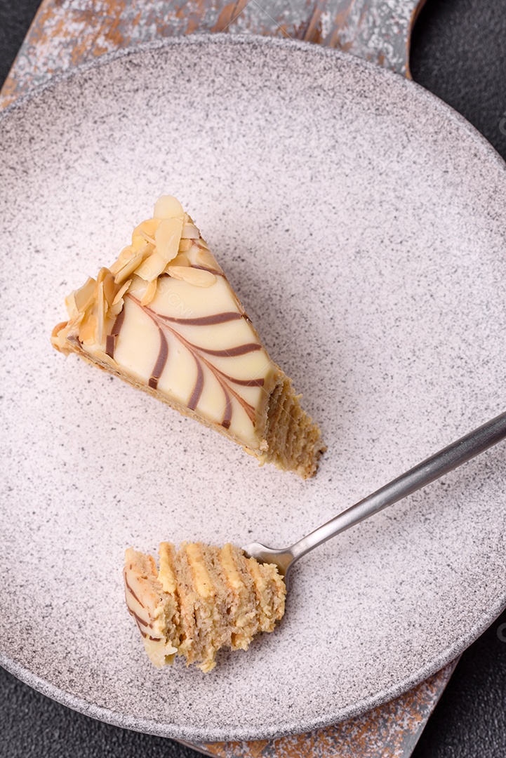 Pedaço de delicioso bolo esterhazy doce com nozes e creme sobre um fundo escuro de concreto