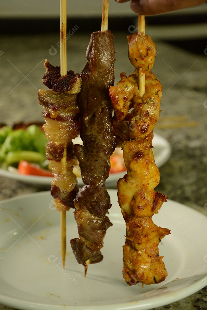 Feche de espetinhos carnes bovina e frango e fundo de salada