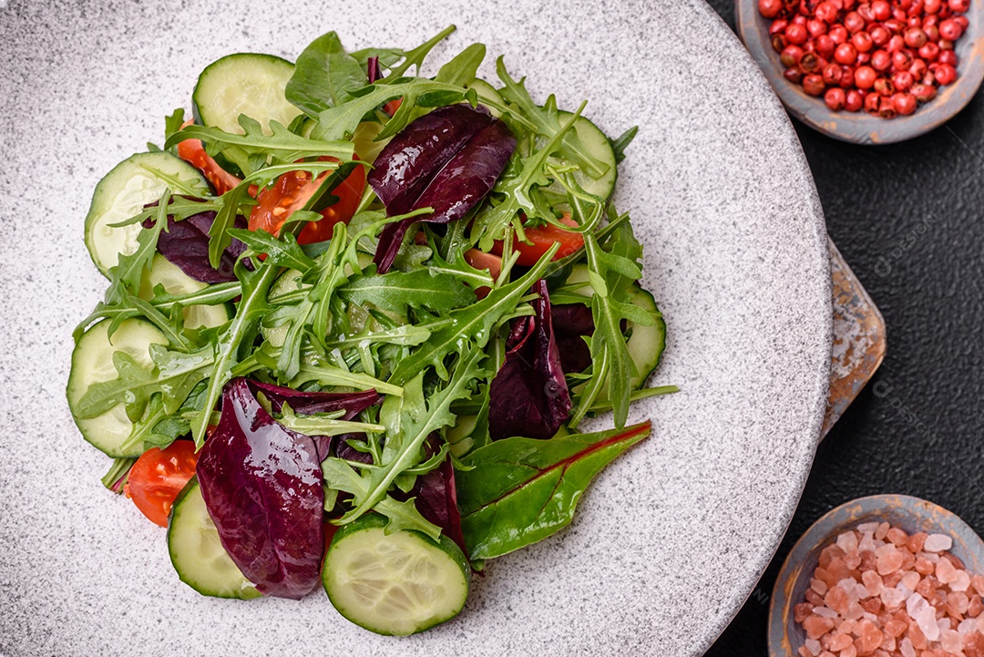 Deliciosa salada suculenta com salmão, tomate, pepino, ervas, sementes de abóbora, sal e especiarias em uma placa cerâmica sobre um fundo escuro de concreto