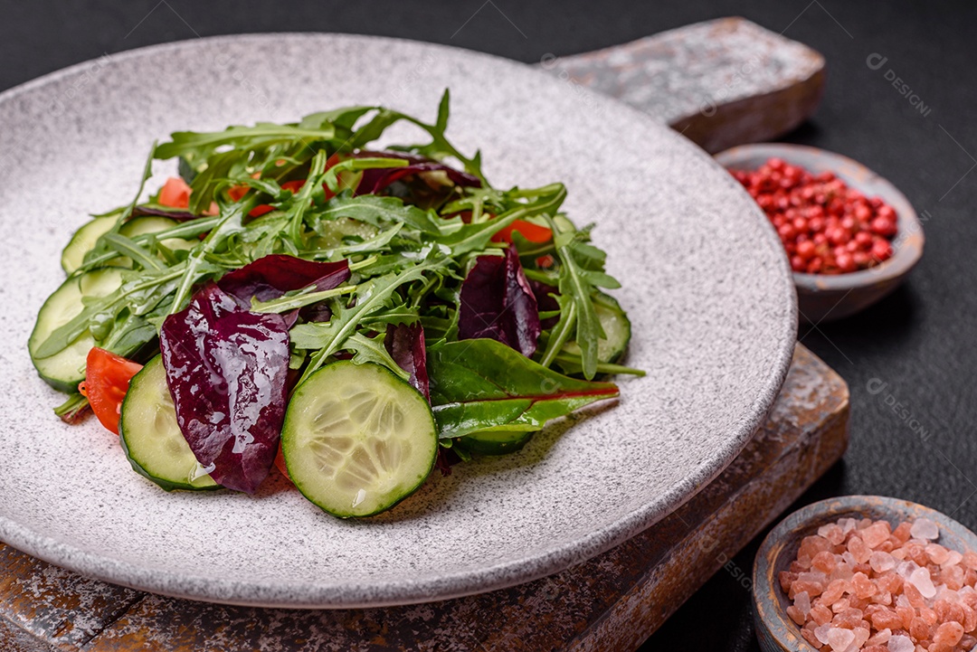 Deliciosa salada suculenta com salmão, tomate, pepino, ervas, sementes de abóbora, sal e especiarias em uma placa cerâmica sobre um fundo escuro de concreto