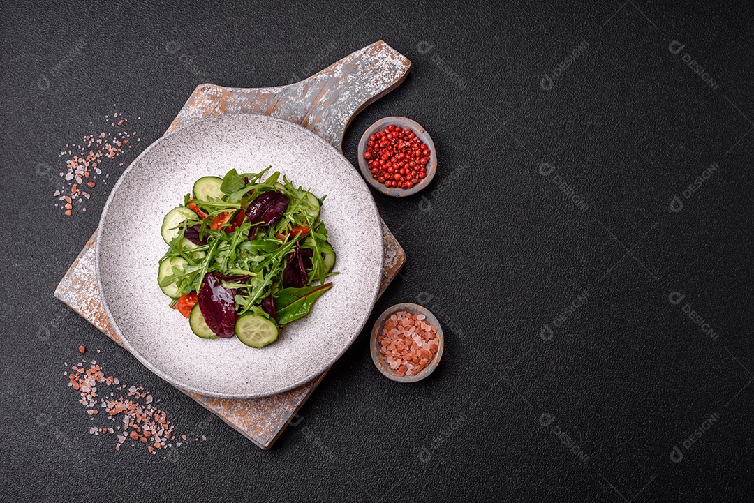 Deliciosa salada suculenta com salmão, tomate, pepino, ervas, sementes de abóbora, sal e especiarias em uma placa cerâmica sobre um fundo escuro de concreto