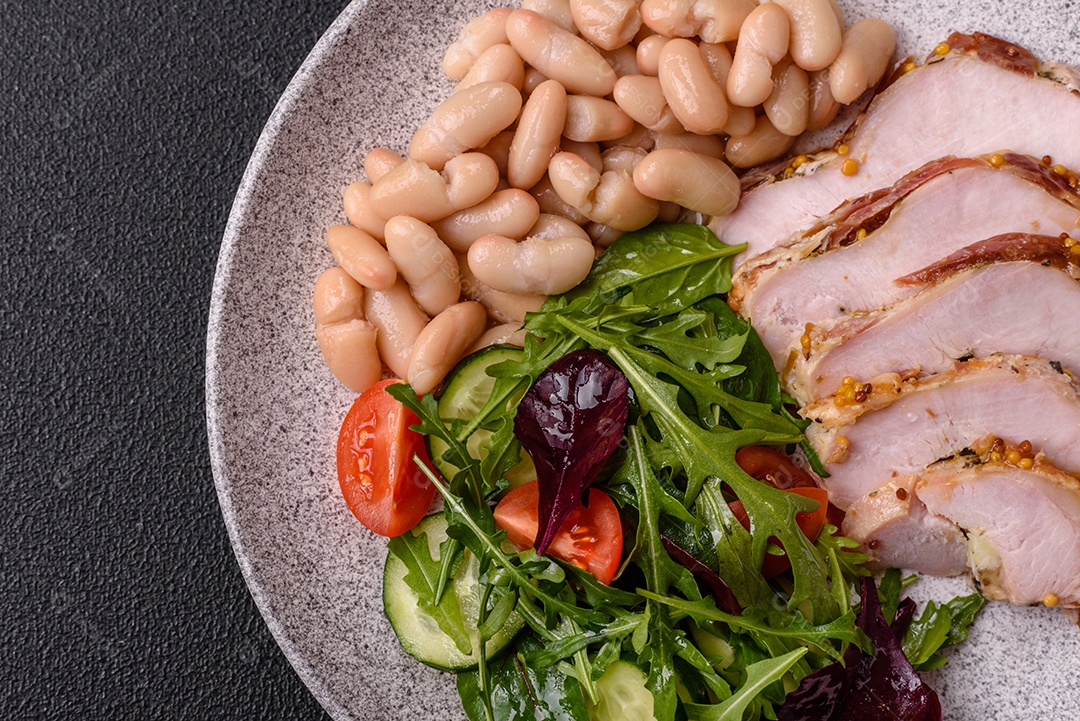 Deliciosa salada suculenta com salmão, tomate, pepino, ervas, sementes de abóbora, sal e especiarias em uma placa cerâmica sobre um fundo escuro de concreto