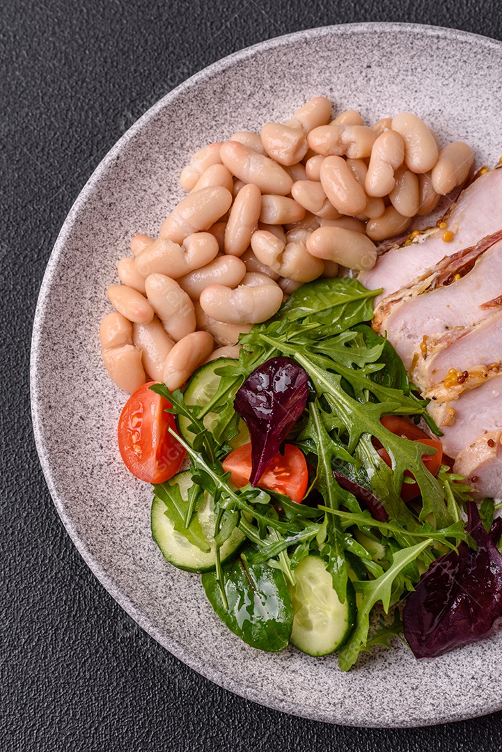 Deliciosa salada suculenta com salmão, tomate, pepino, ervas, sementes de abóbora, sal e especiarias em uma placa cerâmica sobre um fundo escuro de concreto